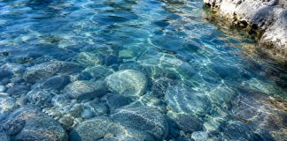 Clear blue water rippling over smooth river stones in natural sunlight