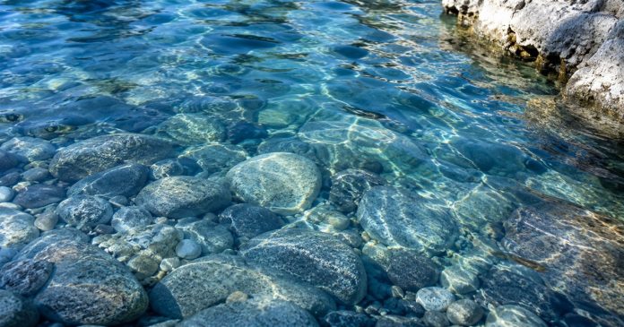 Clear blue water rippling over smooth river stones in natural sunlight