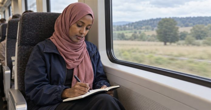Intuition journal realistic cover 4077 Woman in a dusty-rose headscarf writing in a notebook on her lap beside a train window